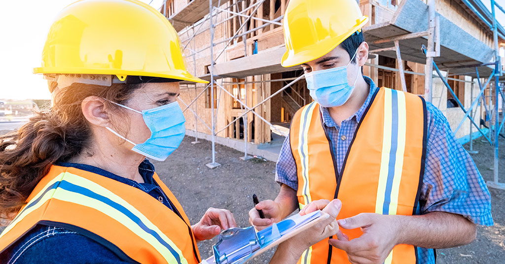 two construction workers with a clipboard while one writes on it.